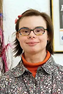 Porträt einer freundlich in die Kamera lächelnden Frau mit kurzen braunen Haaren und einer auffällig bunt gestreiften Brille.