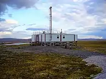 Inmitten einer kargen Landschaft steht ein Containerbau mit einem Holzunterbau.