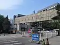 Haupteingang als breiter Torrahmen mit Schriftzeichen des Pekinger Filmakademie und Kontrollhäuschen  in der Mitte der Einfahrt