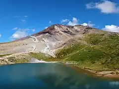Im Vordergrund ist ein Ausschnitt des Sees am Fuße eines Berges zu sehen