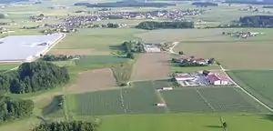 Kirchweidach im Hintergrund, links das Gewächshaus, im Vordergrund eine Photovoltaikanlage, dazwischen der Bohrplatz