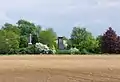 Blick über ein flaches Feld im Frühling 2014 mit dem Denkmal für die Hannoveraner und dem Gordon-Denkmal