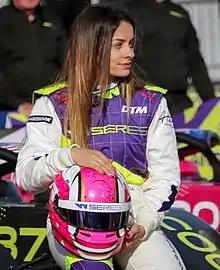 Marta García sitzt in ihrem Rennanzug auf ihrem Rennwagen. Am Schoß hält sie ihren Helm. Sie blickt nach links und hat lange braune Haare.
