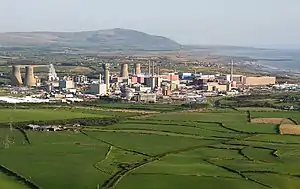 Luftbild der Sellafield-Anlage (2005). Die vier Kühltürme des KKW Calder Hall wurden 2007 abgerissen. Der Abluftturm des Windscale Reaktors 2 wurde bereits 2001 abgerissen. Auf dem Foto ist der ca. 125 m hohe Turm des verunglückten Reaktors 1 noch zu erkennen, welcher sich im aktiven Rückbau (bis ca. 2025) befindet. Die Kugel ist der WAGR, welcher bereits 1981 stillgelegt wurde mit vollständigem Rückbau bis ca. 2005. (Stand 2023).