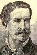 Alexandre Rey Colaço ist im Porträt einer in Sepia gehaltenen Fotografie. Er hat einen Oberlippenbart, der an den Enden zugespitzt verläuft. Sein Haar ist kurz und rechts gescheitelt.