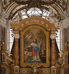 barockes Kircheninterieur, Altar mit gold-roten Säulen, in der Mitte ein monumentales Heiligengemälde, auf dem Ludwig, rot-blau gewandet, und von Engeln umgeben ein Kreuz hält.
