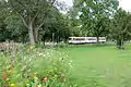 Der dreiteilige MAN-Schienenbus der Osning-Bahn durchquert in der Bahnhofseinfahrt von Bad Laer den Kurpark.