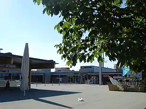 Heutiges Bahnhofsgebäude von Süden her gesehen  mit allen Veränderungen und Anbauten, der Bahnhofsplatz  vorne und der Bushof „Bahnhof Süd“ links