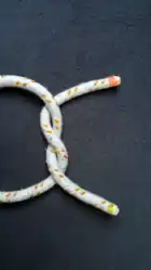 Das Bild 1 von oben um 90° im UZS gedreht.Ein „S“ geschlagener Halber Knoten (Man betrachte die Stelle, an der ein Seil in der Mitte über das andere geht. Das Seil mit rotem Ende zeigt den Buchstaben S).