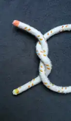 Das Bild 3 von oben um 90° im UZS gedreht.Ein „S“ geschlagener Halber Knoten (das Seil mit gelbem Ende zeigt den Buchstaben S).