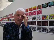 Weißhaariger Mann vor einer Reihe von Bildern