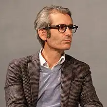 Björn Wilhelm auf einem Podium im karierten Blazer, kritischer Gesichtsausdruck, Halbprofil, 2023