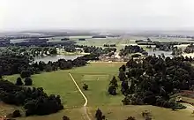 Farbfotografie in der Obersicht von einem Schloss inmitten der Landschaft. Links und rechts des Gebäudes liegen zwei Seen. Viele Felder, Wiesen und kleine Waldgruppen sind im Umkreis.