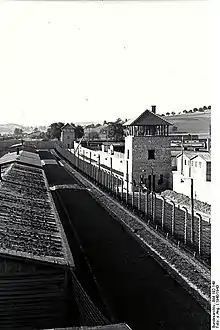 Steinerne Wachtürme, steinerne Mauer und Stacheldrahtzaun. Baracke im Vordergrund