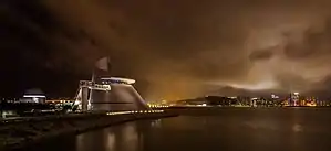 Eine Aufnahme bei Nacht zeigt das Science Center vor einem beleuchteten Horizont. Im Vordergrund ist ein Fluss zu sehen.