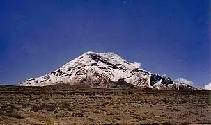 Ein schneebedeckter Berg in der Ferne unter einem klaren, blauen Himmel. Das Gelände im Vordergrund ist sehr öd.