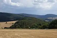 Der Berg Burg von Nordwesten gesehen. Links am Bildrand der Berg Windhain, darüber lugen die Türme des Großen Feldbergs hervor, mittig am Horizont Kleiner Feldberg, sowie davor der Weilsberg, der nach links in den Hühnerberg übergeht, hinten rechts der Glaskopf über den Häusern von Oberems sowie wiederum darunter Wüstems.