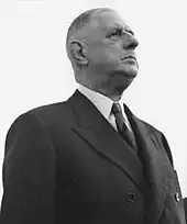 Der französischen Staatspräsident Charles de Gaulle. Das Schwarzweißfoto von 1961 zeigt ein Brustbild des etwa 70-Jährigen vor hellem Hintergrund, mit ernstem Blick, vermutlich im Freien. Er ist bekleidet mit weißem Hemd und dunklem Jackett oder Mantel.