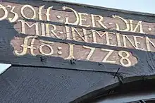 Teil eines Spruchbalkens (s. https://de.wiktionary.org/wiki/Spruchbalken) mit der kontrahierenden Abbreviatur „Aō:17Z8“ (für „Anno [domini] 1728“, dt. „Im Jahre des Herrn 1728“)