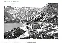 historische Schwarz-Weiss-Aufnahme aus dem Jahr 1894, Schrägaufnahme eines zweigeschossigen Gebäudes, der Douglasshütte; Seitenwand wirkt grober als Fassade; im Hintergrund der Lünersee