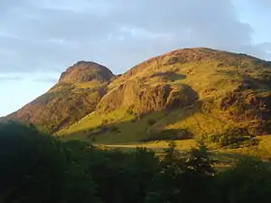 Ein etwas zerklüfteter, mit Gras bewachsener Berg im Licht des Sonnenuntergangs.