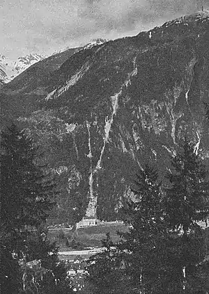 Blick von der rechten Reusstalseite oberhalb Amsteg auf die Zentrale und die Druckleitung des Kraftwerks Arniberg. Der Pfeil weist auf die ungefähre Lage des Arnisees hin.