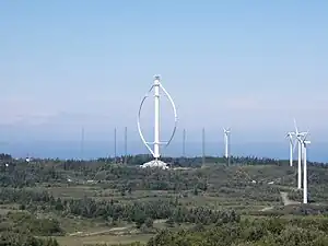 Der Darrieusrotor Éole. Seine Größe wird im 
Vergleich mit den Bäumen und den anderen Windrädern ersichtlich.