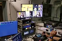 Verschiedene technsche Geräte mit Monitoren auf einem grauen Tisch, am unteren rechten Rand des Bildes sind die Hände einer Veranstaltungstechnikers zu sehen, eine davon greift eine Art Joystick an einem Mischpult