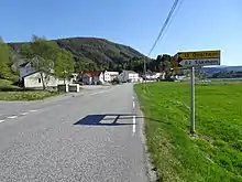 Foto einer Straße die an einigen Häusern vorbeiführt. Im Hintergrund eine Erhebung