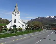 Foto einer Straße und einer weiß gestrichenen Holzkirche in bergiger Landschaft
