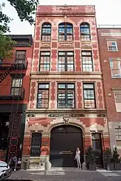 Viergeschossiges historisches Gebäude mit Backstein-Sandstein-Fassade und dunkelbraunen oder -grauen Fenstern und dem großen Rolltor der früheren einständigen Fahrzeughalle