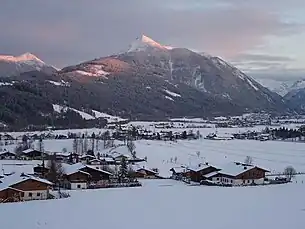 Die Flachau, Blick vom Taleingang nach Südost. Im Vordergrund Reitdorf, dahinter Feuersang und ganz hinten rechts Flachau Ort. Links im Hintergrund der Strimskogel, mittig und das Bild dominierend der Lackenkogel (halblinks und weiter im Vordergrund sein bewaldeter Nebengipfel Koppen), rechts, ganz im Hintergrund, der Hauptkamm der Radstädter Tauern.