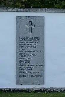 Grauer Gedenkstein an einer weißen Mauer mit den eingemeißelten Namen der am 9. April 1945 in Flossenbürg ermordeten Mitglieder des Widerstandes: Dietrich Bonhoeffer, Wilhelm Canaris, Ludwig Gehre, Hans Oster, Karl Sack, Theodor Strünck
