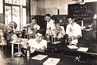 Chemieunterricht in der Schulgemeinde Wickersdorf, ca. 1934/35. Lt. Tafel beschäftigen sich Schüler und Lehrer u. a. mit einer Reaktionsgleichung, bei der es darum geht, dass eine stärkere Säure die schwächere aus ihrem Salz verdrängt