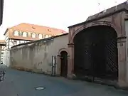 Eingangsportal und Umfassungsmauer des ehemaligen Adelshofes mit Blick entlang der heutigen Brunnengasse (im Bild links) Richtung Osten. Die vorbildlich als Wohnhaus restaurierte ehemalige Scheune (im Hintergrund) gehörte früher mit zum Anwesen.
