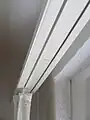 Eine weiße zweiläufige Gardinenschiene mit Gardine. Hier ohne Kölner Brett.