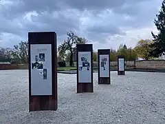 Auf hellem Untergrund sind die Stelen mit Biografien der Ermordeten zu sehen. Sie bestehen aus Metall, dass braun verrostet ist.