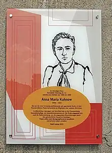 Die Gedenktafel ist an einer hellen Sandsteinwand des Gebäudes angebracht. Sie ist in den Farben weißrot und orange gestaltet und zeigt Anna Maria Kuhnow mit schwarzer Tusche gezeichnet.