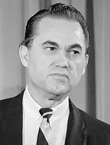 Ein Foto von George Wallace im mittleren Alter mit einem schwarzen Anzug und einer Krawatte.