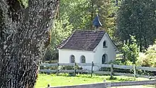 Kapelle in weiß mit Glocke auf Dach, davor ein Zaun