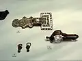 Aus einem Mädchengrab (Grab 438): Bronzefibel, gegossene silberne Bügelfibel (Typ Nocera Umbra), kreisaugenpunzierte, pyramidenförmiger Ohrringe; Ende 6./Anfang 7. Jahrhundert.