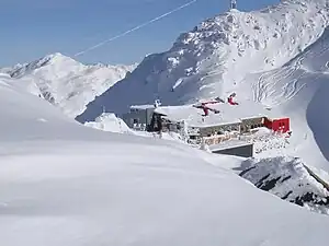 Glungezerhütte vom Grat zur Sonnenspitze, dahinter Seile und Stütze einer Seilbahn des Bundesheers, im Hintergrund der Malgrübler