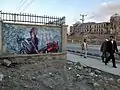 Ein fertiges Graffiti an einer Mauer ist zu sehen. In der rechten Bildhälfte laufen Passanten vorbei und schauen es an.