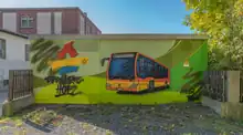 Das Foto zeigt die Ansicht eines Stromhäuschens mit einem Graffito, das einen Hofer Stadtbus und Text und Textlogo der Stadtwerke Hof zeigt