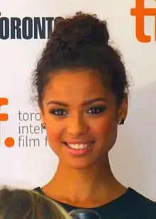 Gugu Mbatha-Raw steht vor einer weißen Wand mit der grauen Aufschrift toronto international film festival. Weiter oben steht das Wort Toronto in schwarzen Buchstaben sowie ein weiteres, abgeschnittenes Wort in orangen Buchstaben. Mbatha-Raw trägt ein dunkelblaues Oberteil, je einen goldfarbenen Ohrstecker in jedem Ohr sowie ihre schwarzen Haare als Hochsteckfrisur. Vor ihr sind der Kopf und das Mikrofon eines Reporters teilweise zu sehen.