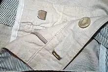 Metallfarbener Hosenhaken und Öse an einer hellen Herrenhose