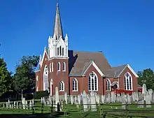 Eine Backsteinkirche mit einem weißen Turm und einem Friedhof im Vordergrund