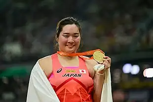 Haruka Kitaguchi präsentiert mit strahlendem Gesicht und Tuch über dem Rücken ihre Goldmedaille.