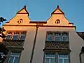 Doppelgiebel mit Pinienzapfen; gotisierenden Vorhangbogen und Blendmaßwerk in den Brüstungsflächen; ovale Bodenfenster
