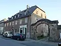 Ehemaliger Gasthof (ohne östlichen Anbau) mit drei Wirtschaftsgebäuden, Hofpflasterung und Torbogen, vor dem Gasthof drei achteckige Granitpfeiler